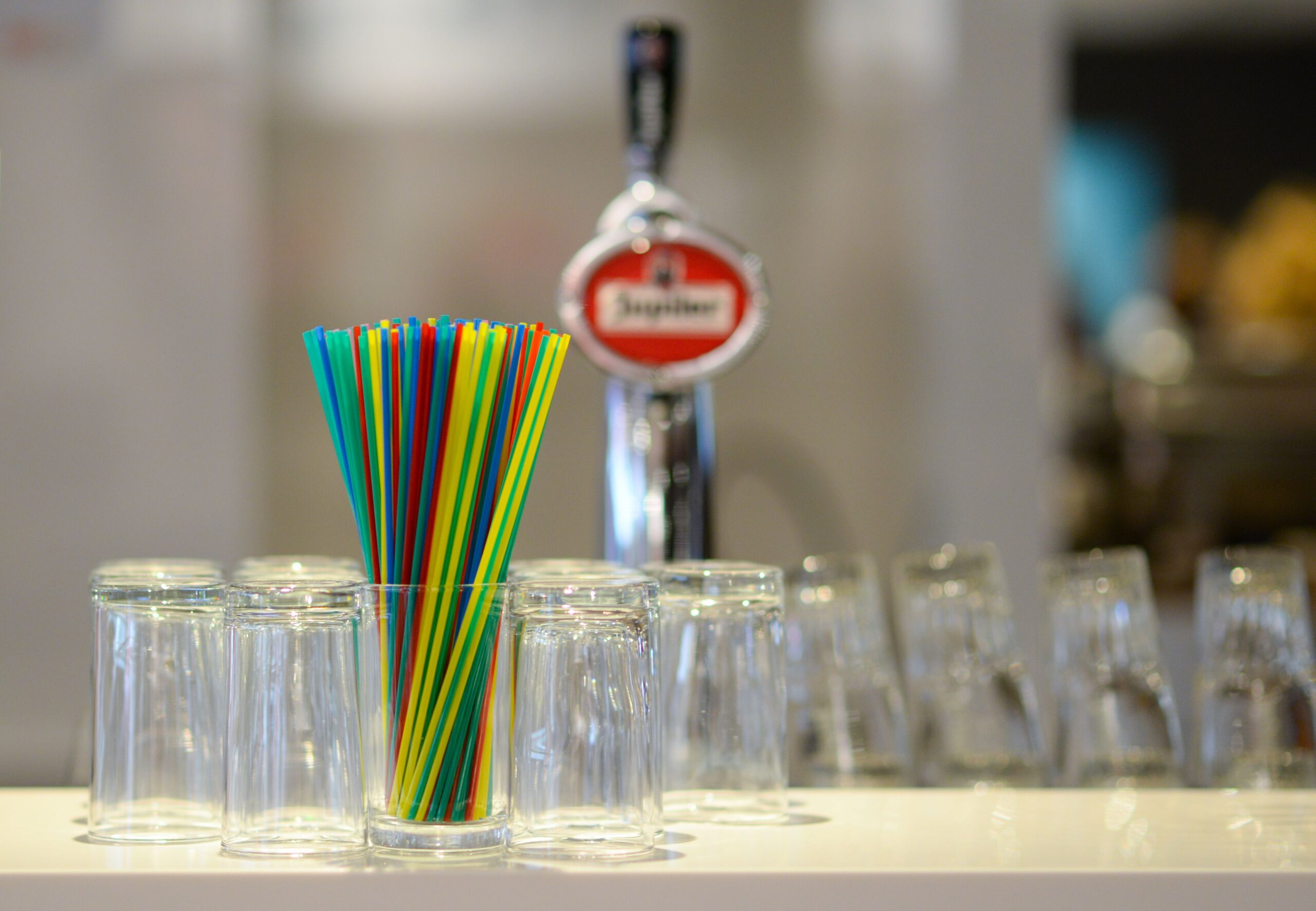 Vibrant straws and upside-down glasses on a bar counter with blurred background.