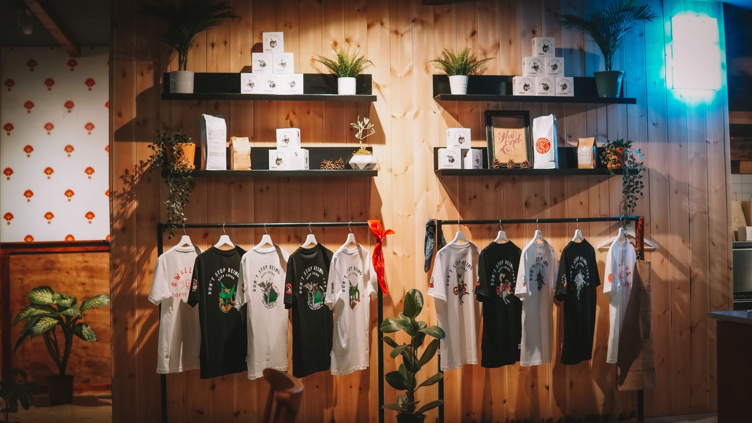 pexels photo 14146828 14146828 Stylish T-shirt display in a cozy, modern retail store with plants and wooden decor.