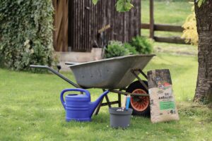 A serene backyard gardening scene featuring a wheelbarrow, watering can, and potting soil on grass.