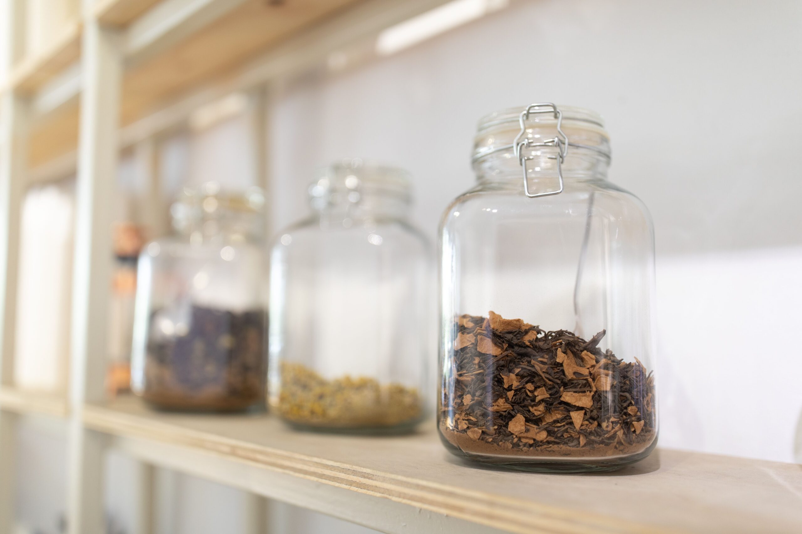 Close-up of glass jars filled with dried herbs on a wooden kitchen shelf.